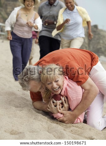 Happy couple playing American Football with friends in background at beach