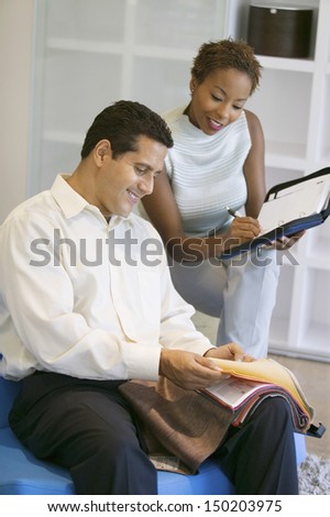 Middle aged saleswoman assisting man in selecting fabrics at furniture store