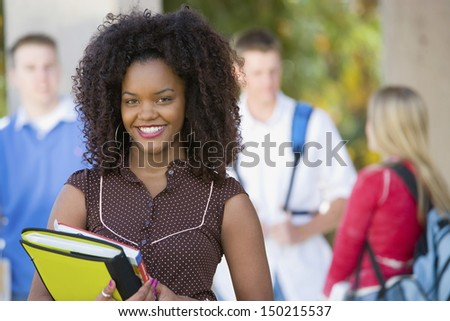 Portrait of smiling African American female student on college campus with classmates in background