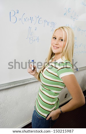 Portrait of beautiful student solving algebra equation on whiteboard in classroom