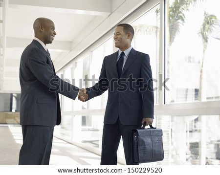 Happy businessmen shaking hands while standing in office corridor