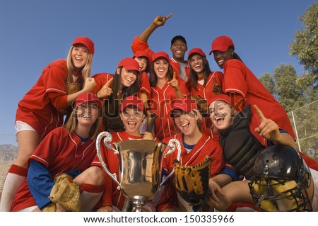 Low angle portrait of successful female softball team and coach with trophy celebrating against blue sky