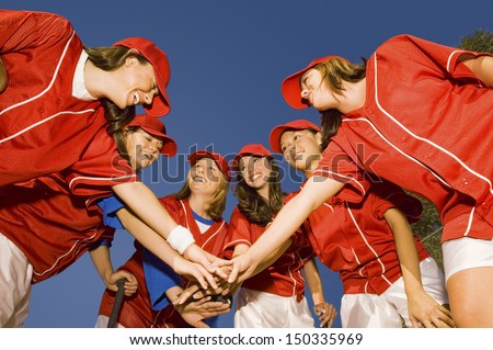 Happy female softball players stacking hands against clear blue sky