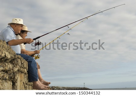 Side view of happy senior couple fishing against cloudy sky