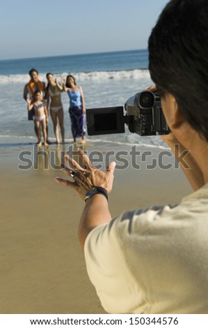 Middle aged man filming family on beach
