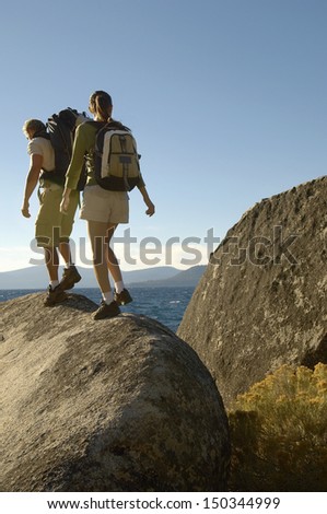 Full length rear view of hiking couple walking on boulder at coast