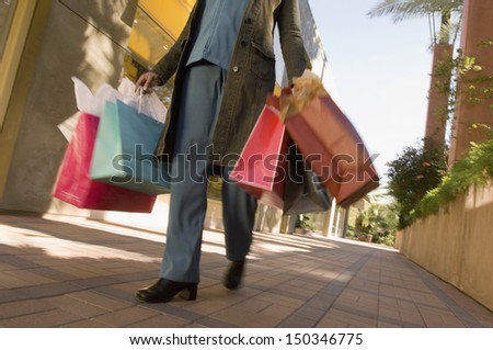 Low section of woman with shopping bags walking on pavement