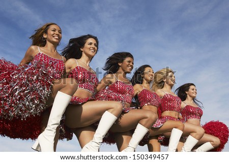 Row of multiethnic cheerleaders doing high kick against cloudy sky