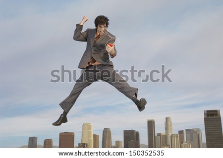 Full length of young businessman listening to MP3 player above cityscape