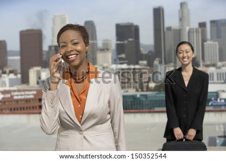 Smiling African American businesswoman on call with colleague holding briefcase against cityscape