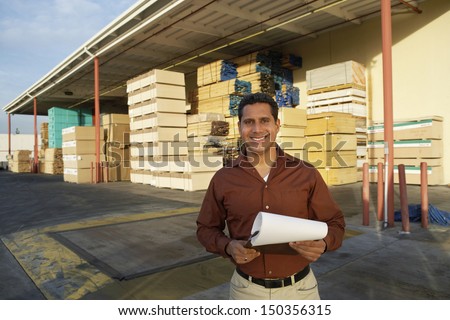 Portrait of happy middle aged man with clipboard standing in front of timber factory