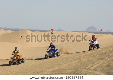 Three men riding quad bikes in desert