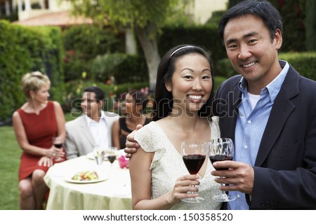 Portrait of happy Asian couple toasting wine with friends in background
