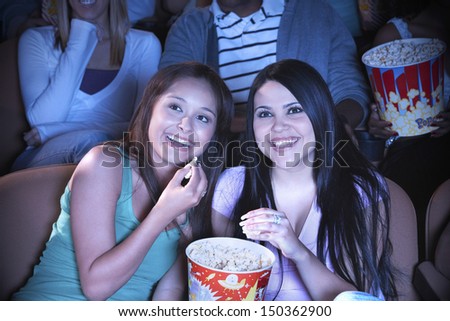 Young friends eating popcorn while watching film in movie theater