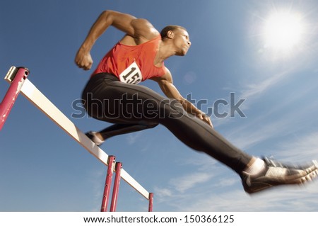 Low Angle View Of Determined Male Athlete Jumping Over A Hurdles