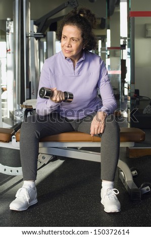 Full length of senior woman looking away while lifting weight in health club