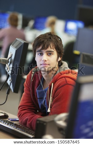 Portrait of a male university student using computer while listening to music in college