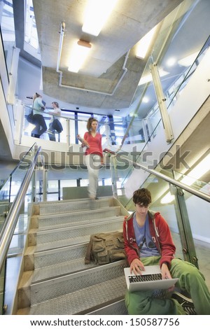 University student using laptop on staircase with friends behind