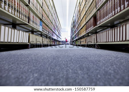Distance shot of a female in university library with shelves of books in foreground