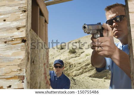 Man watching colleague aiming hand gun at firing range