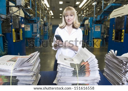 Portrait of a smiling woman with calculator and stacks of newspapers in the factory
