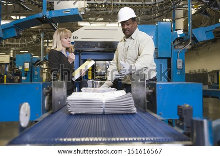 Side view of a woman by man working on newspaper production line in newspaper factory
