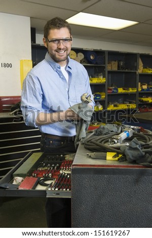 Portrait of a smiling young man with tools working in workshop