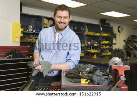 Portrait of a smiling young man with tools working in workshop