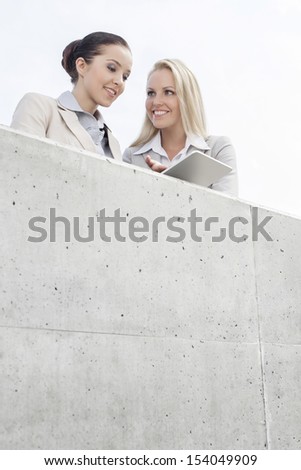 Low angle view of smiling business executives using digital tablet on office terrace against sky
