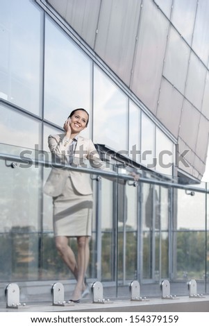 Full length of happy young businesswoman using cell phone at office balcony
