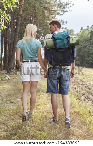 Rear view of young hiking couple holding hands while walking in countryside