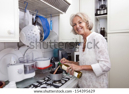 Portrait of senior woman adding olive oil to saucepan at kitchen counter