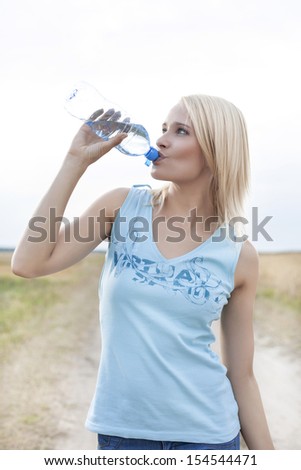 Young woman drinking water from bottle on field