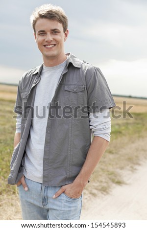 Portrait of handsome young man with hands in pockets standing on field
