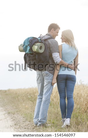 Rear view of romantic hiking couple looking at each other while standing at field