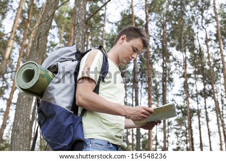 Side view of young man with backpack reading map in woods