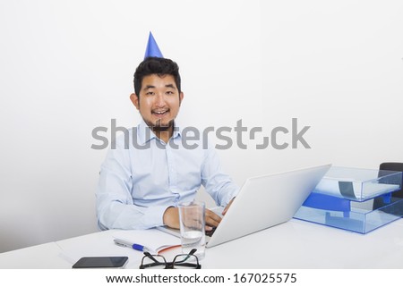 Portrait of happy businessman wearing party hat sitting at desk in office