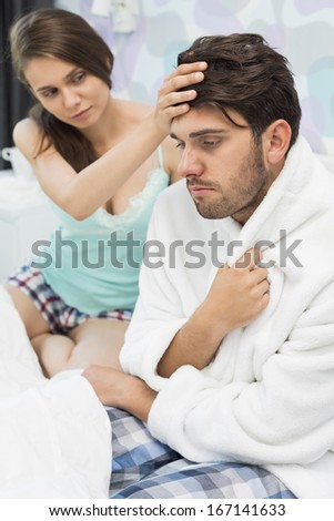Young woman checking man\'s temperature on bed