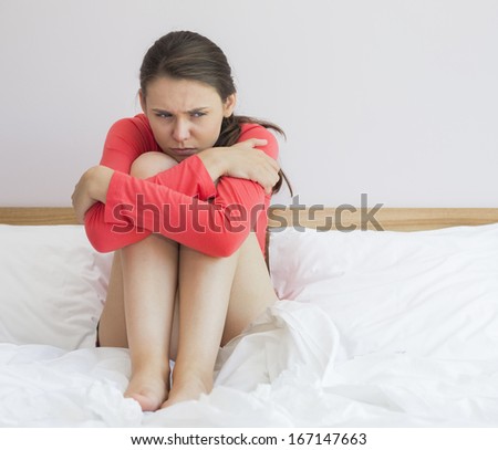 Sad woman hugging knees on bed at home