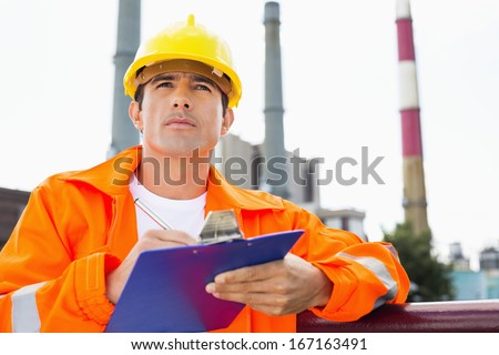 Male construction worker writing on clipboard at industry