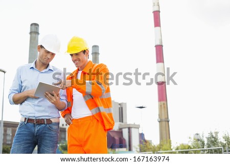 Two construction workers discussing over tablet PC at industry