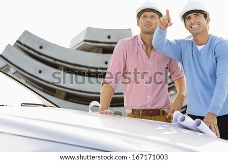 Architects with blueprints on car discussing at construction site