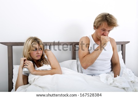 Scared woman looking at man coughing in bed