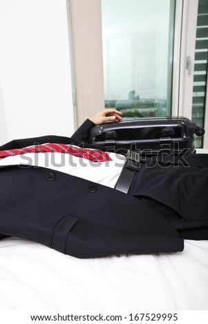 Midsection of businessman with luggage lying in bed at home