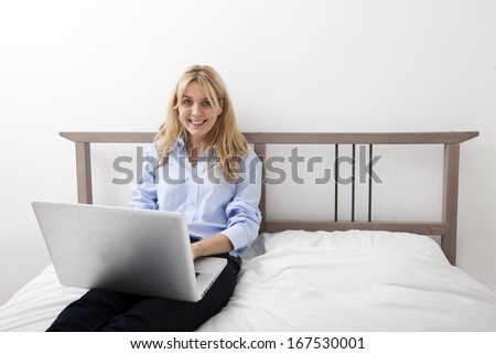 Portrait of happy businesswoman using laptop in bed