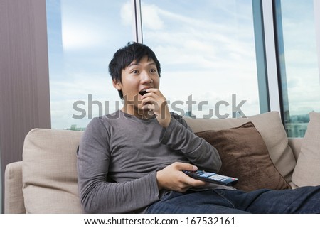 Surprised mid-adult man watching television on sofa at home