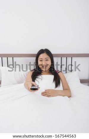 Portrait of smiling woman changing channels with remote control in bed