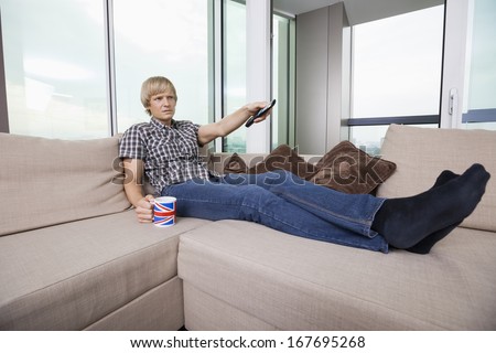 Relaxed mid-adult man watching television while having coffee on sofa at home