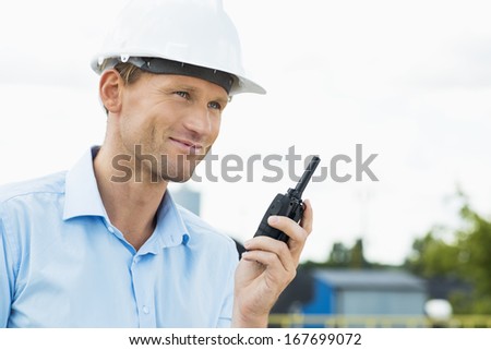 Smiling architect holding two way radio at construction site
