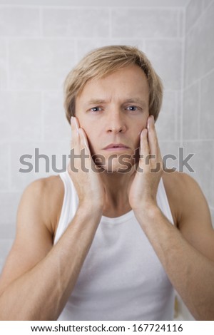 Portrait of man applying aftershave moisturizer in bathroom